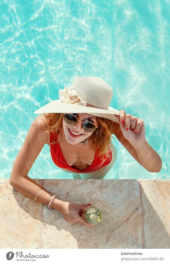 Young woman in red swimsuit and straw hat with tropical cocktail mojito pool water Summer caucasian Swimming pool Fashion blue turquoise alone Happy smile