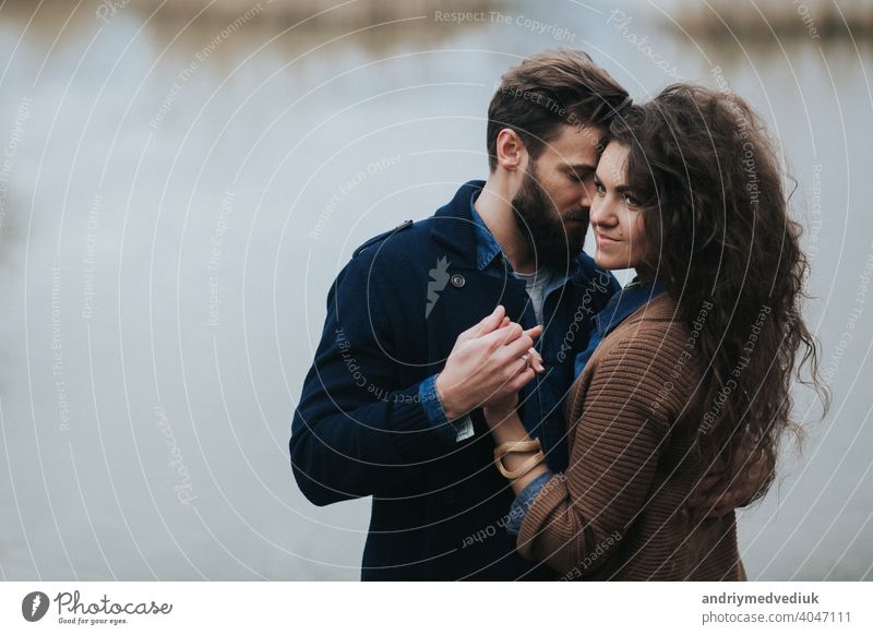 Happy lovers near the lake. Young couple is hugging on autumn day outdoors. A bearded man and curly woman in love. Valentine's Day. Concept of love and family.