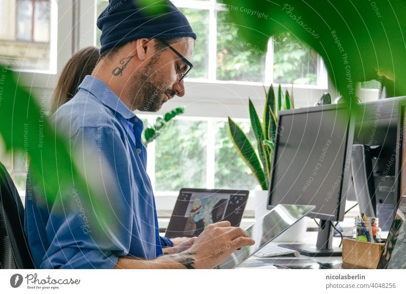 Young man with tattoo working on laptop in office Freelance work Computer Use of the laptop Hipster Technology Wireless Millennia more adult people masculine
