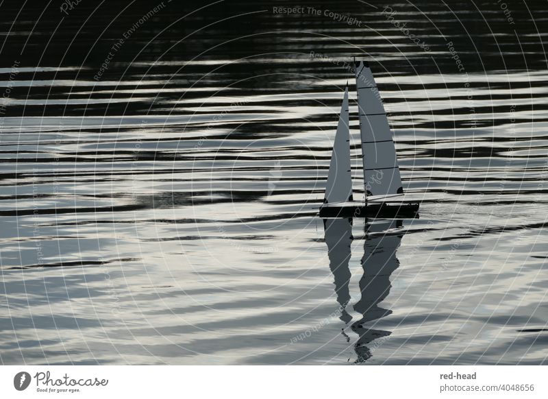 small sailboat, model boat from the side, reflection of the sails in the water, horizontal lines through light waves Sailboat Model ship Surface of water