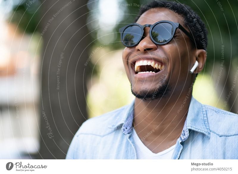African american man smiling while walking outdoors. african sunglasses city urban concept ear buds smile joy leisure summer enjoy earbud casual earpods young