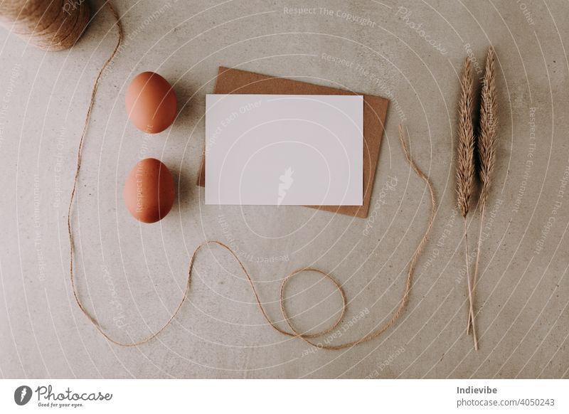 Blank white paper with two eggs, string line and dried grass on grey stone background. Easter greeting card or menu list concept. Flat lay, top view. easter