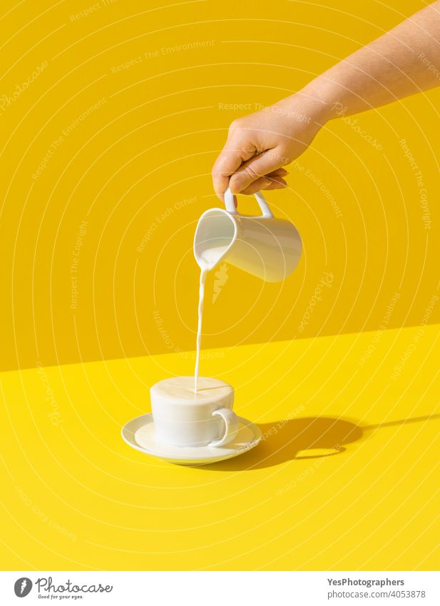 Pouring milk in a cup, on yellow background. Milk overflow from a cup abundance beverage breakfast bright calcium carafe colored colorful colors concept