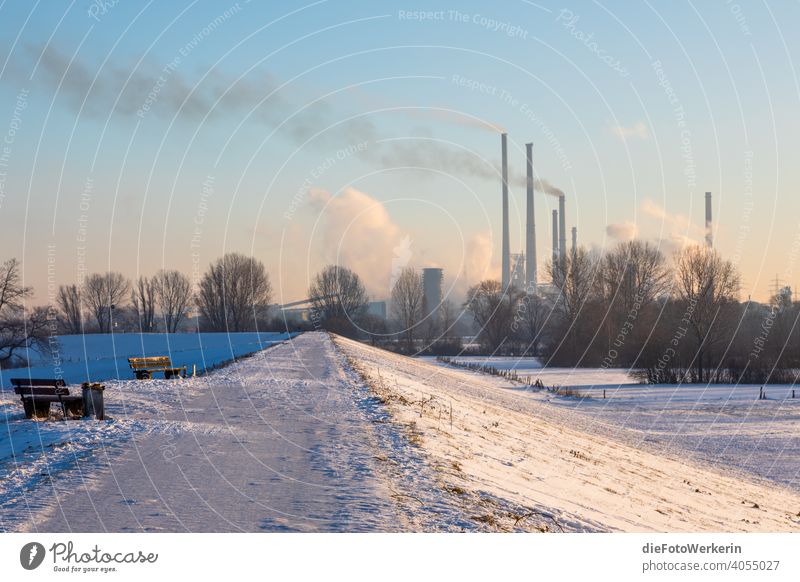 View over a snowy dike to industry Bench Dike Traffic lane Vanishing lines Bright Sky Industry Nature Snow Sunrise technology off Winter Clouds steam smoke
