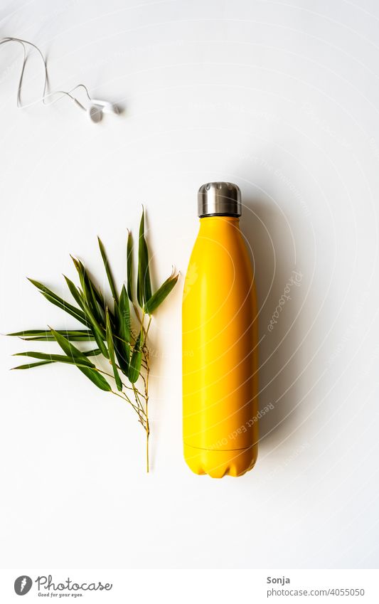 A yellow water bottle and a branch of bamboo on an isolated white background Bottle of water Yellow Reusable Headphones Bamboo Fitness Ecological concept Thermo