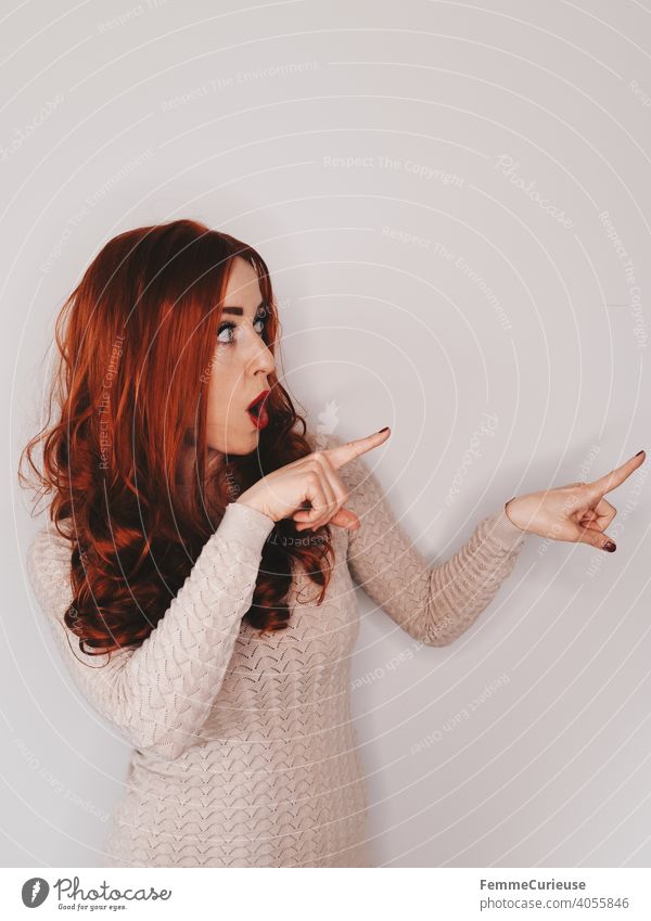 Woman with long red curly hair points with both hands index fingers at something in half profile Half-profile Red-haired red hair Indicate Sweater
