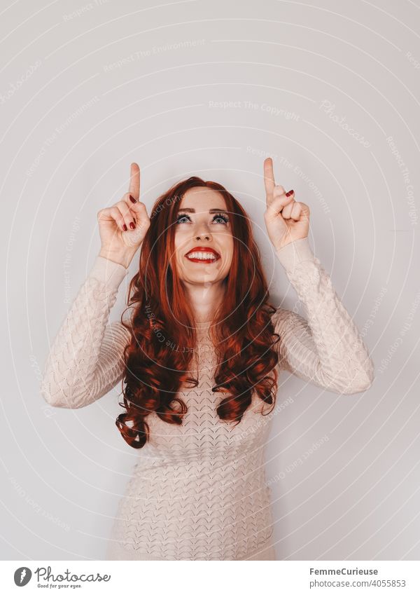 Woman with long red curly hair looks up and also points up with both hands and index fingers upstairs Indicate Interpret Clue Forefinger Hair and hairstyles