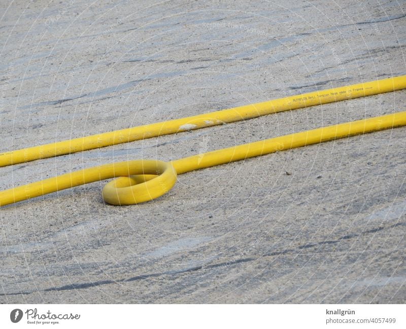 Yellow water hose with loop Water hose Construction site noose looping Hose Garden hose Exterior shot Ground Lie Side by side Parallel two Round Gray