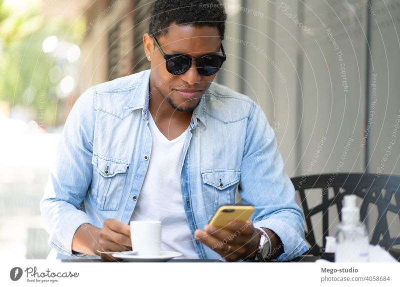 Man using his mobile phone at coffee shop. man urban city african american technology smartphone social media smile joy sunglasses enjoy device network wireless