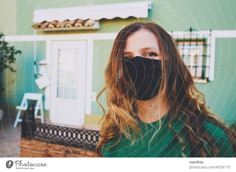 Young woman wearing a black face mask against an urban green wall coronavirus headshot casual life real real people colorful warm warmth lifestyle long hair