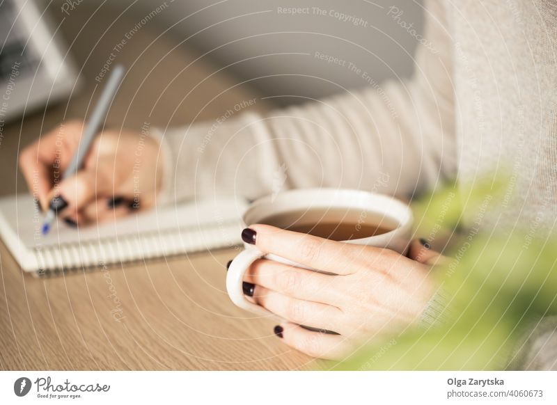 Woman holding a cup of tea in one hand and she is writing. woman working pen cosy drink close up caucasian break lifestyle girl morning comfort day adult