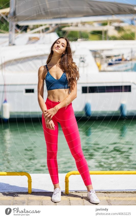 Fitness model in red sportswear outfit posing on waterfront harbour. woman fitness girl female activity training workout young shorts leisure jogger caucasian