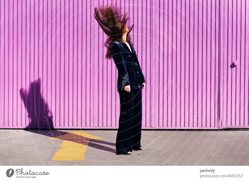 Woman wearing blue suit posing near pink shutter, moving her hair. woman hairstyle fashion model building blind fuchsia purple girl person lifestyle female