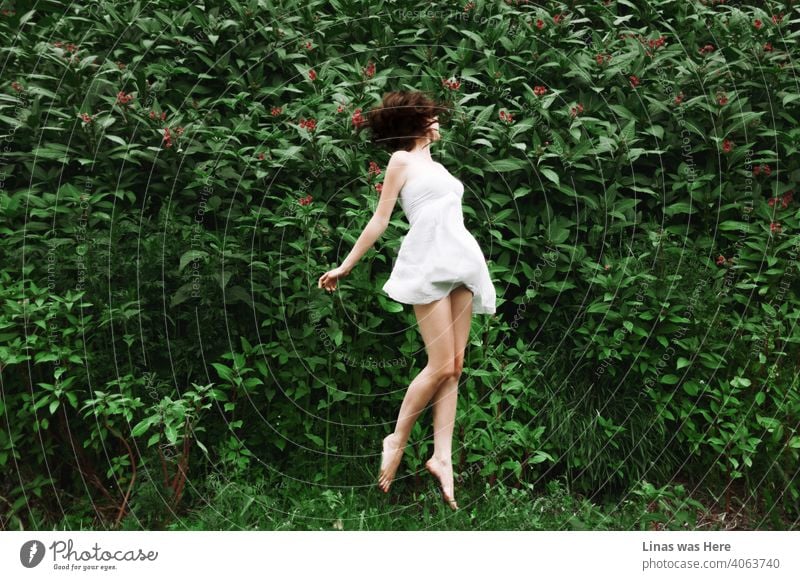 All is green, all is beautiful. A gorgeous brunette girl is jumping into the air joyfully. Dressed in light and white dress she enjoys summertime. The beauty of her long and sexy legs is also truly visible in this image.