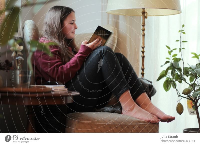 Teen sits on a comfy wingback chair and reads a book Teenage Girls teenager Reading Reading a book reading forms Barefoot barefoot cosy home coziness Cozy