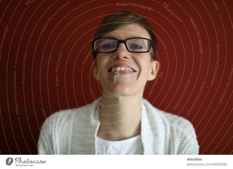 Close portrait of smiling young woman in front of red wall Woman Young woman Slim jeans Top Eyeglasses sits Shoulders Skin Large Athletic Articulated inside