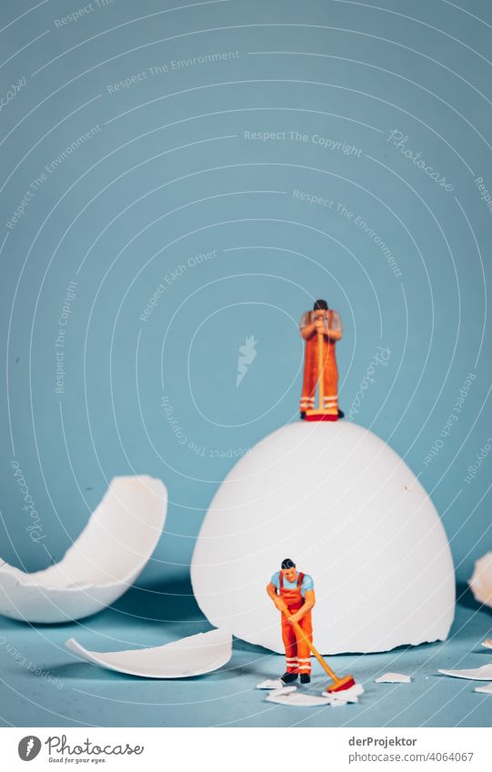 Cleaner stands on an egg while another figure sweeps up the shells of a broken egg Miniature Minimalistic fake Artificial Artistic Easter egg hunt eggs Eggshell