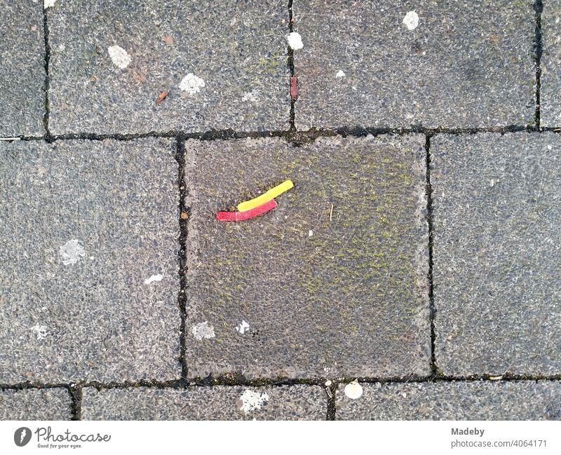 Lakritzstreifen in Gelb und Rot auf grauen Steinplatten mit Kaugummiresten auf einem Platz in Offenbach am Main in Hessen Streifen rot gelb künstlich bunt