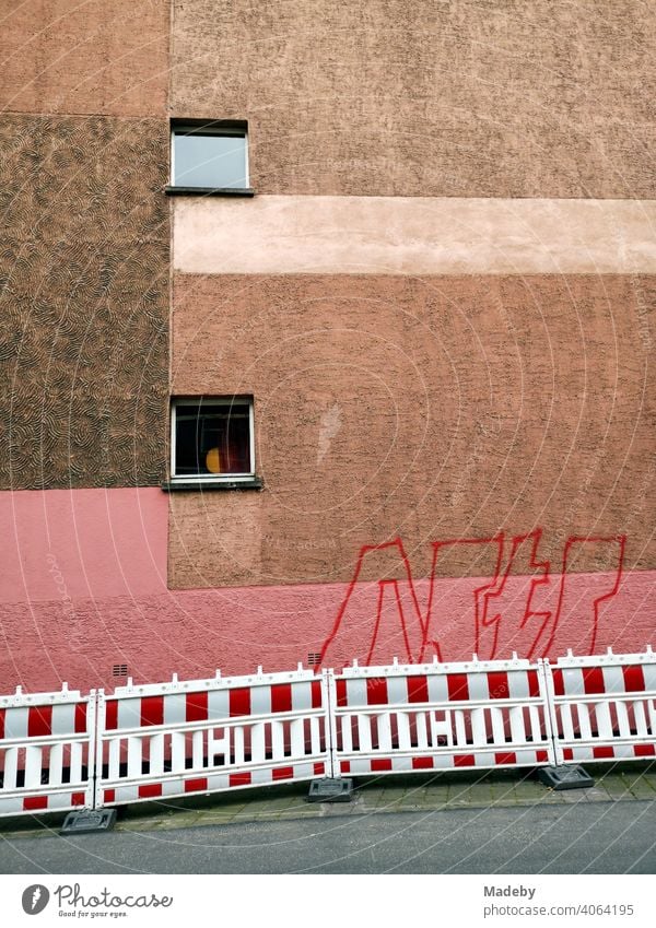 Facade with two windows and colour design in pink and brown tones with graffiti and construction fence in Offenbach am Main in Hesse Paintwork Plaster Colour