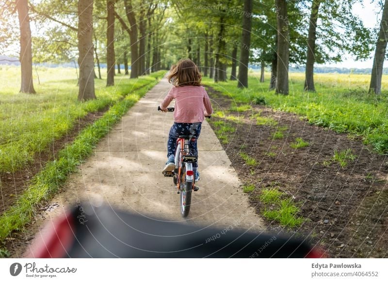 Little girl cycling in the countryside family safety people girls children kids biking bike cycle Europe Holland Netherlands Outdoor nature back rear view grass