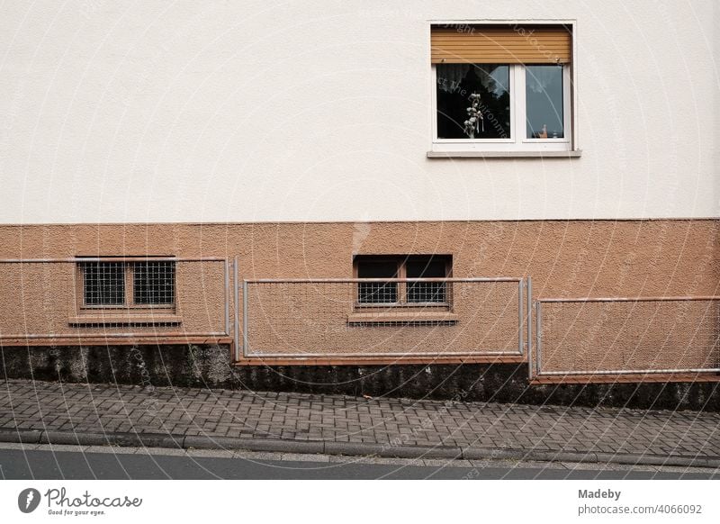 Sidewalk with fence on a sloping street and facade of a residential house with window and roller shutter in Wettenberg Krofdorf-Gleiberg near Giessen in Hesse, Germany