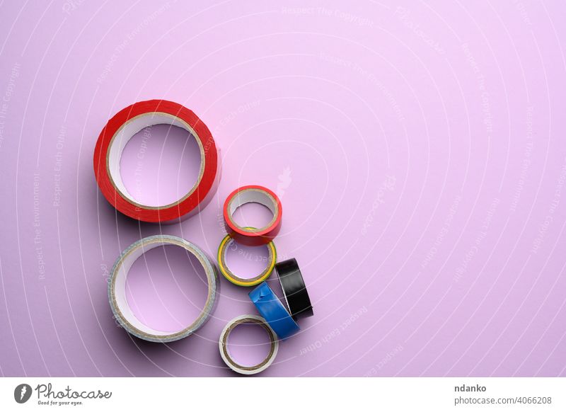 various skeins of multicolored scotch tape and electrical tape on a purple background, top view rubber sellotape sticky supply tool adhesive black blue duct fix