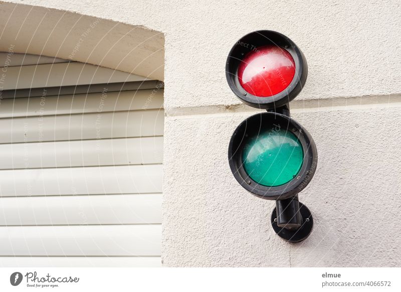 small red and green signal lamps on the house wall next to a closed garage entrance with roller door / traffic light Traffic lights Highway ramp (entrance)