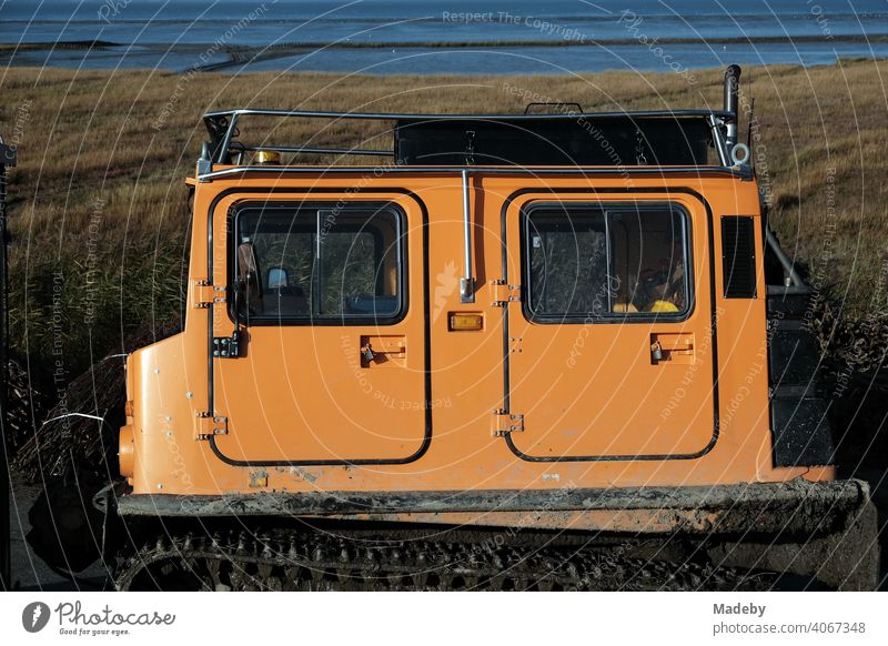 All-terrain tracked vehicle with double cab in bright orange for coastal protection in the Hernst in the mudflats in Bensersiel near Esen on the coast of the North Sea in East Frisia in Lower Saxony