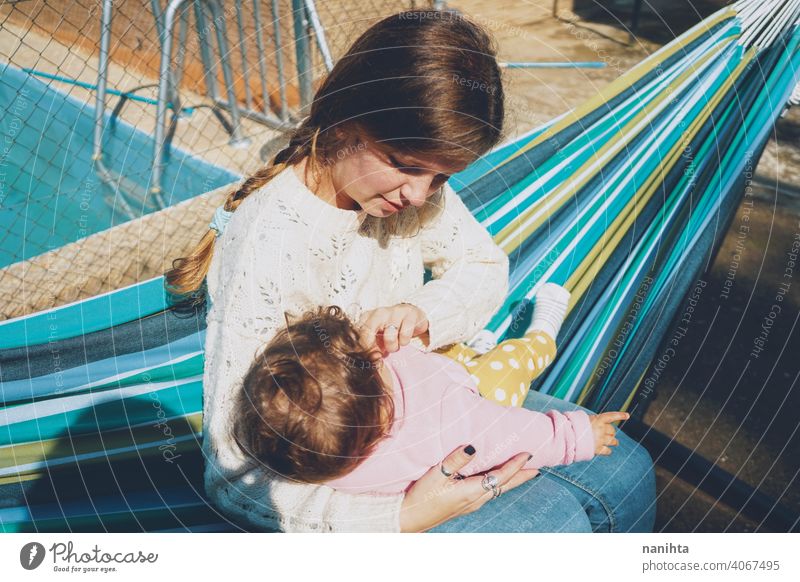Young woman caring her baby sitting on a hammock mom family holidays care love home outdoors day care pool hug daytime routine happiness lovely cute babyhood