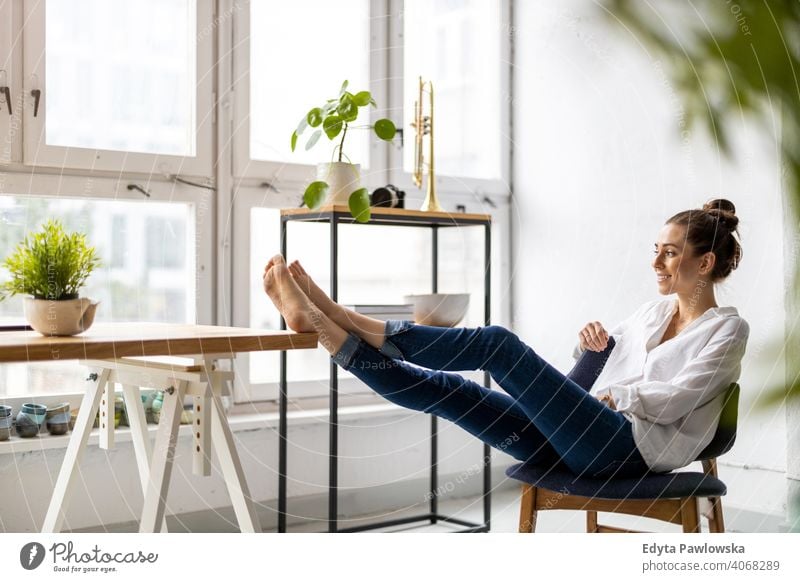 Young woman relaxing in office with her bare feet on desk millennials student hipster indoors loft window natural girl adult one attractive successful people