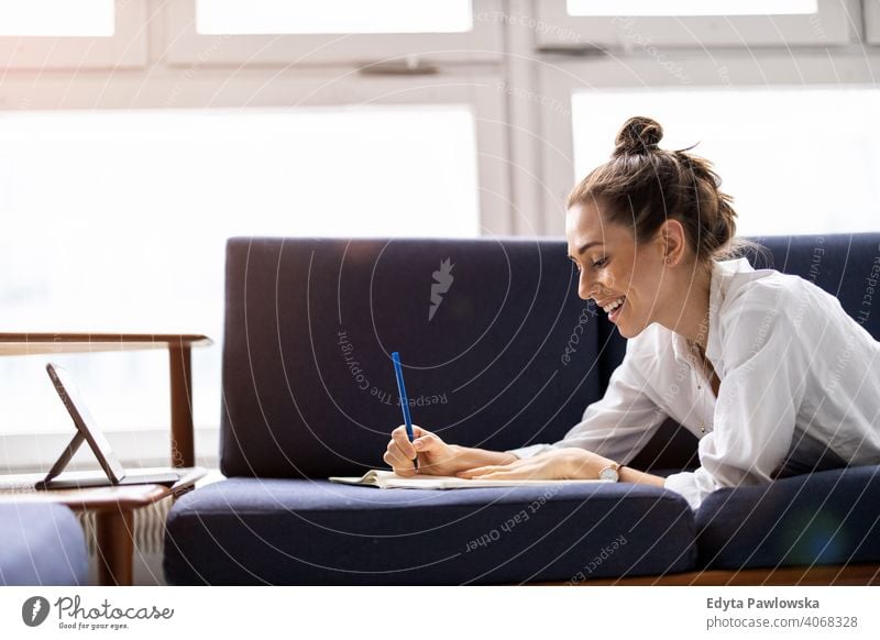 Young woman doing homework on sofa sitting couch resting relaxing comfortable millennials student hipster indoors loft window natural girl adult one attractive