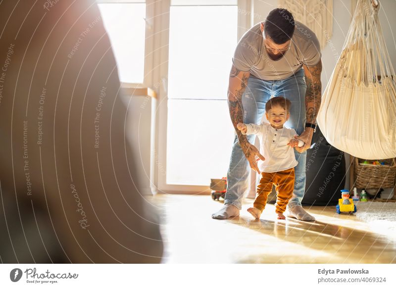 Little boy learning to walk with his father next to him at home single parent single dad fathers day fatherhood stay at home dad paternity leave modern manhood