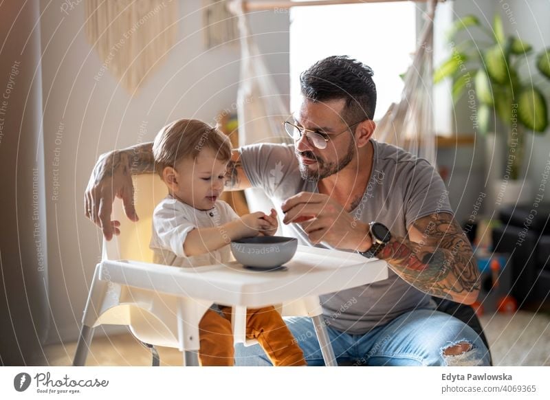 Single dad feeding his baby who is sat in a high chair single parent single dad fathers day fatherhood stay at home dad paternity leave modern manhood family