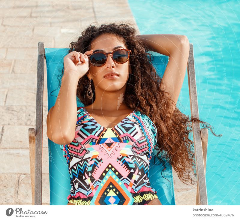 Young woman in one-piece swimsuit relaxing near a swimming pool red tropical water Summer caucasian Fashion alone Garden Outdoor Exotic Sensual hispanic