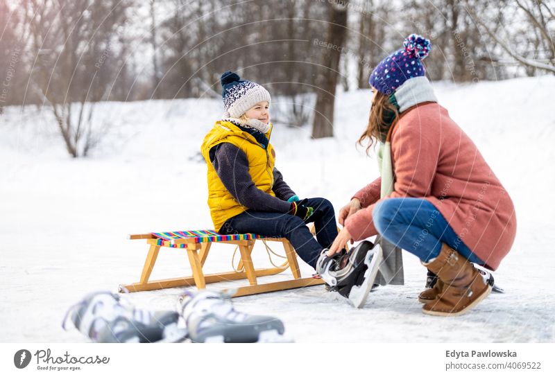 Mother helping son to put on his ice skates mother daughter season together frozen cheerful fun kid people park holiday forest childhood woman girl nature joy