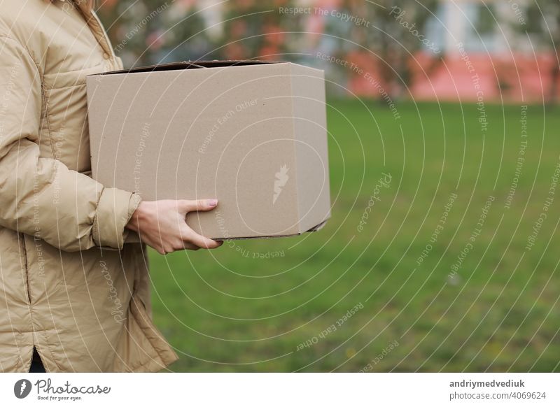 Cropped Delivery girl hold empty cardboard box outdoors on a residential complex background. Service coronavirus. Online shopping. mock up. delivery service
