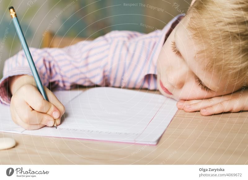 Kid writing in a notebook and lying on the desk. kid boy study little tired sleeping doing cute blond pink shirt pencil copybook school face one day homework