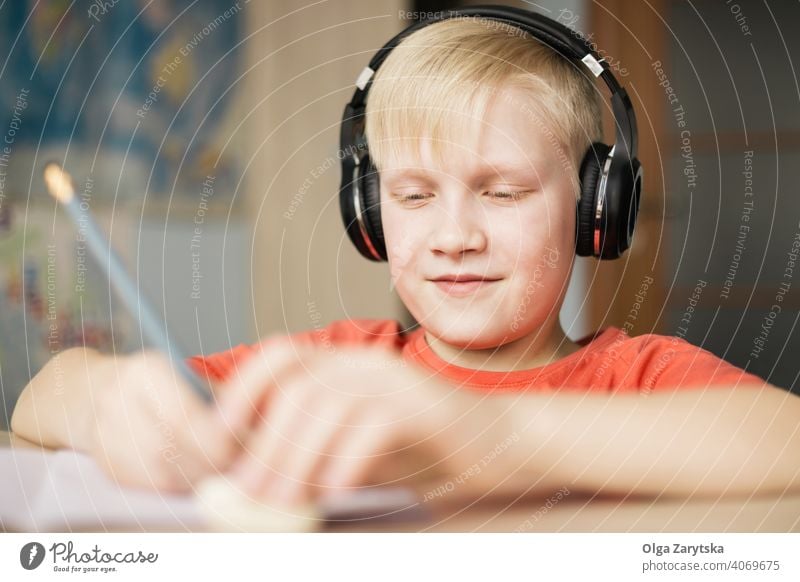 Boy in headphones writing and smiling. boy kid child indoor cute smile homework fun write caucasian blond hand pencil hair face person childhood music listening