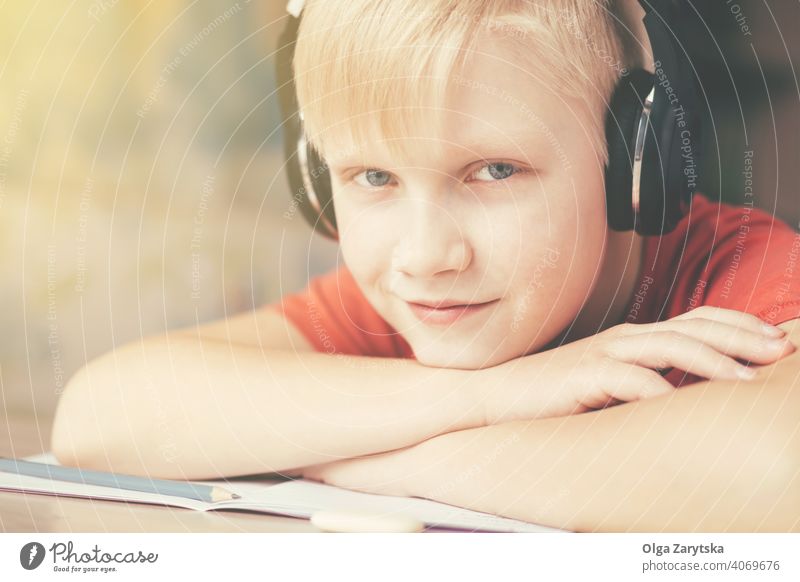 Blondy teenage boy in headphones resting and listening to music . smiling kid indoor cute smile gray eye homework fun caucasian blond hand pencil hair face