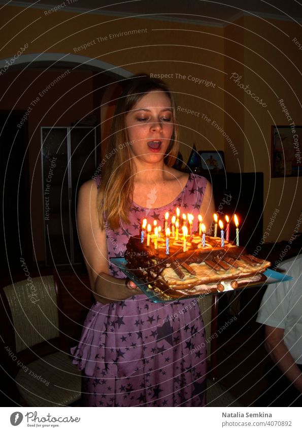 Young girl in lilac dress holding handmade festive cake in piano shape with burning candles in her hands in dark room. Birthday celebration at home. Vertical orientation.