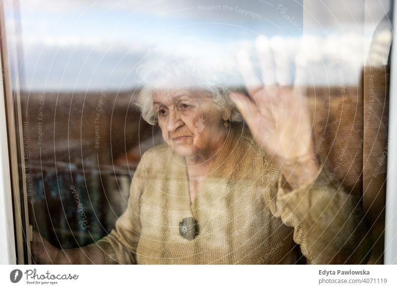 Senior woman looking out of window at home covid lockdown coronavirus quarantine looking through window social distancing glass vulnerable waiting despair tired