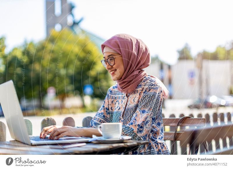 Young Muslim woman using a laptop in outdoor cafe hijab headscarf muslim islam arabic summer girl people young adult female lifestyle active outdoors millennial