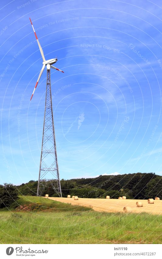Wind turbine stands on a field with straw bales Wind energy plant Pinwheel Renewable energy Environment co2 Autumn Field harvest season Bale of straw Blue sky