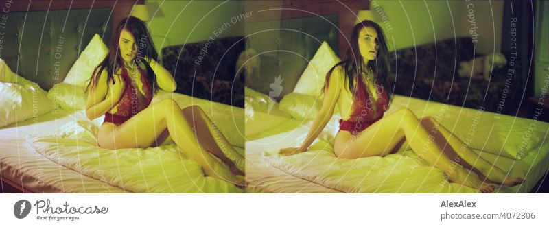 Analogue double exposure with young woman in red lingerie in hotel bed in yellow-green light, in the background a small white dog on the couch - film transport error