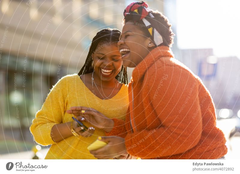 Happy female friends sending messages with their smartphones in the city diversity diverse people love outdoors day positivity confident carefree woman adult