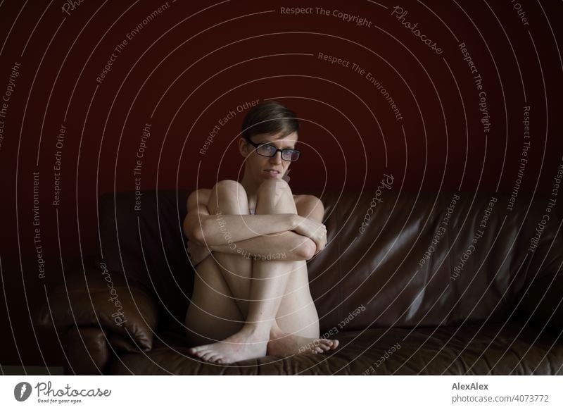 Portrait of a young woman on a brown leather couch Woman Young woman Slim Top Eyeglasses sits Skin Large Athletic Articulated inside Room studio Bright daylight