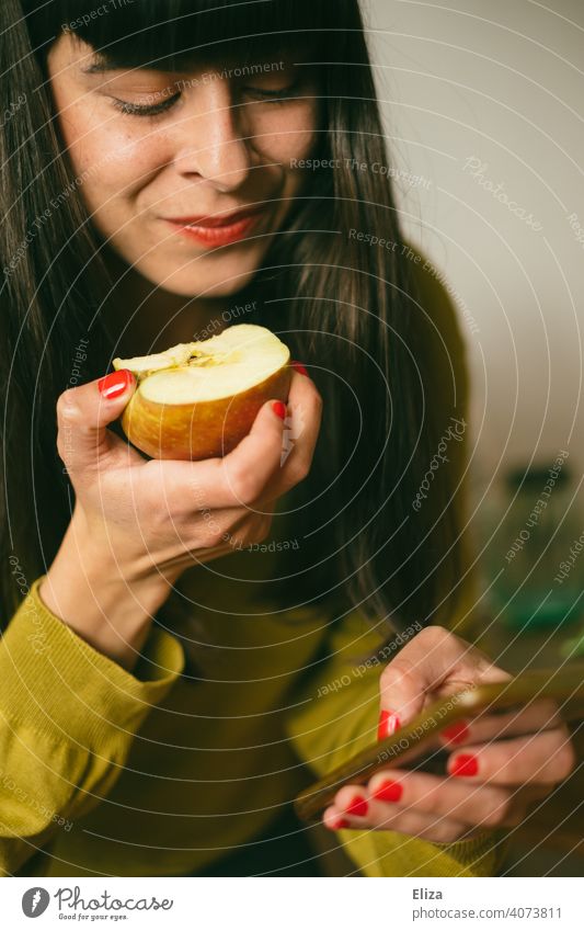A woman eats an apple while busy with her smartphone Telephone Cellphone Eating Apple Healthy Eating fruit Snack snack Online by the way Woman