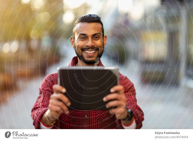 Young man using digital tablet outdoors at urban setting Sinhalese asian Indian bearded outside street standing city Warsaw one casual lifestyle guy attractive
