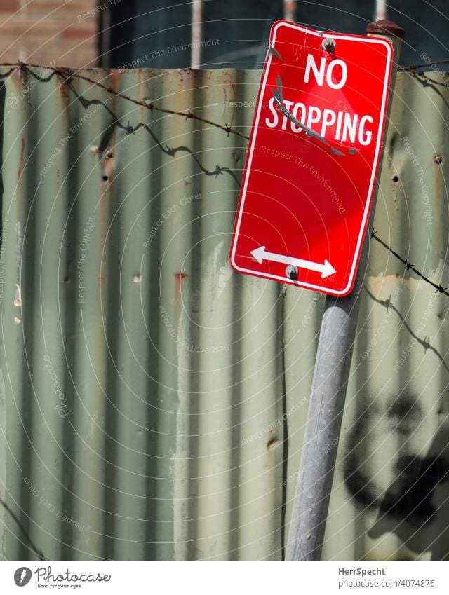 No stopping sign in front of corrugated iron Road sign Signs and labeling Characters Road traffic Deserted Colour photo English Arrow Barbed wire