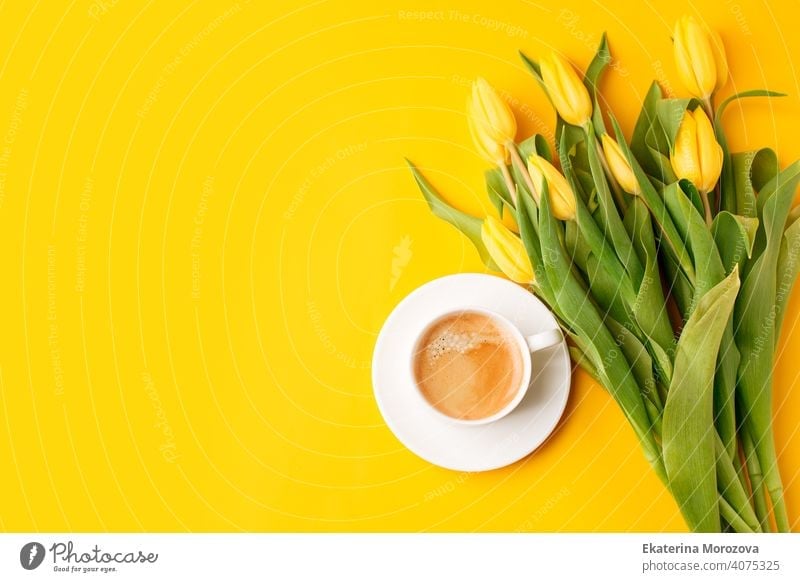 Beautiful spring breakfast on Mothers or Womans International day 8 march. Bouquet of yellow tulips and coffee cup on bright yellow table top view. Flat lay, stylish banner for site, seasonal flyer
